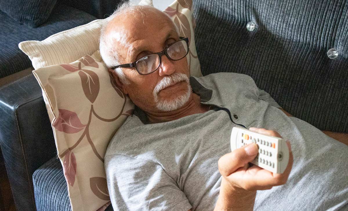 senior man lying on the couch with a remote, leading a sedentary life