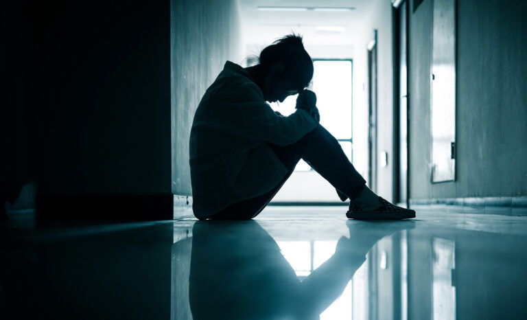 Stressed teen sitting on the floor of a school hallway with her head lowered