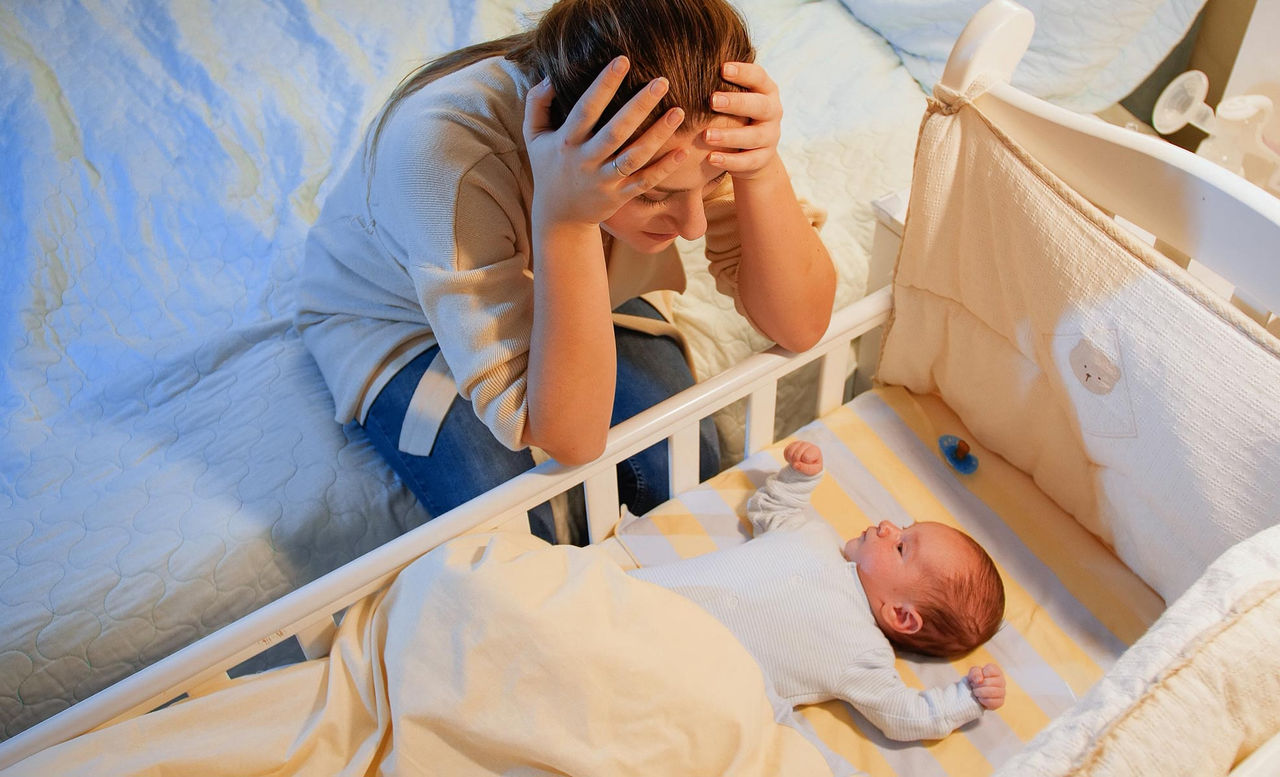 Stressed mother sitting beside her baby's crib