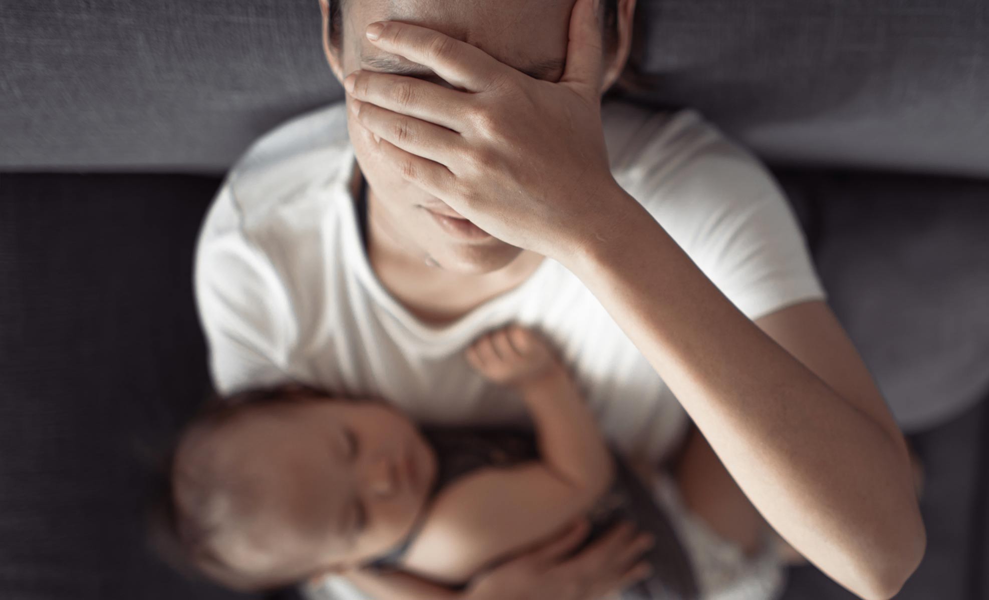 Young mother holding her baby while covering her eyes in stress