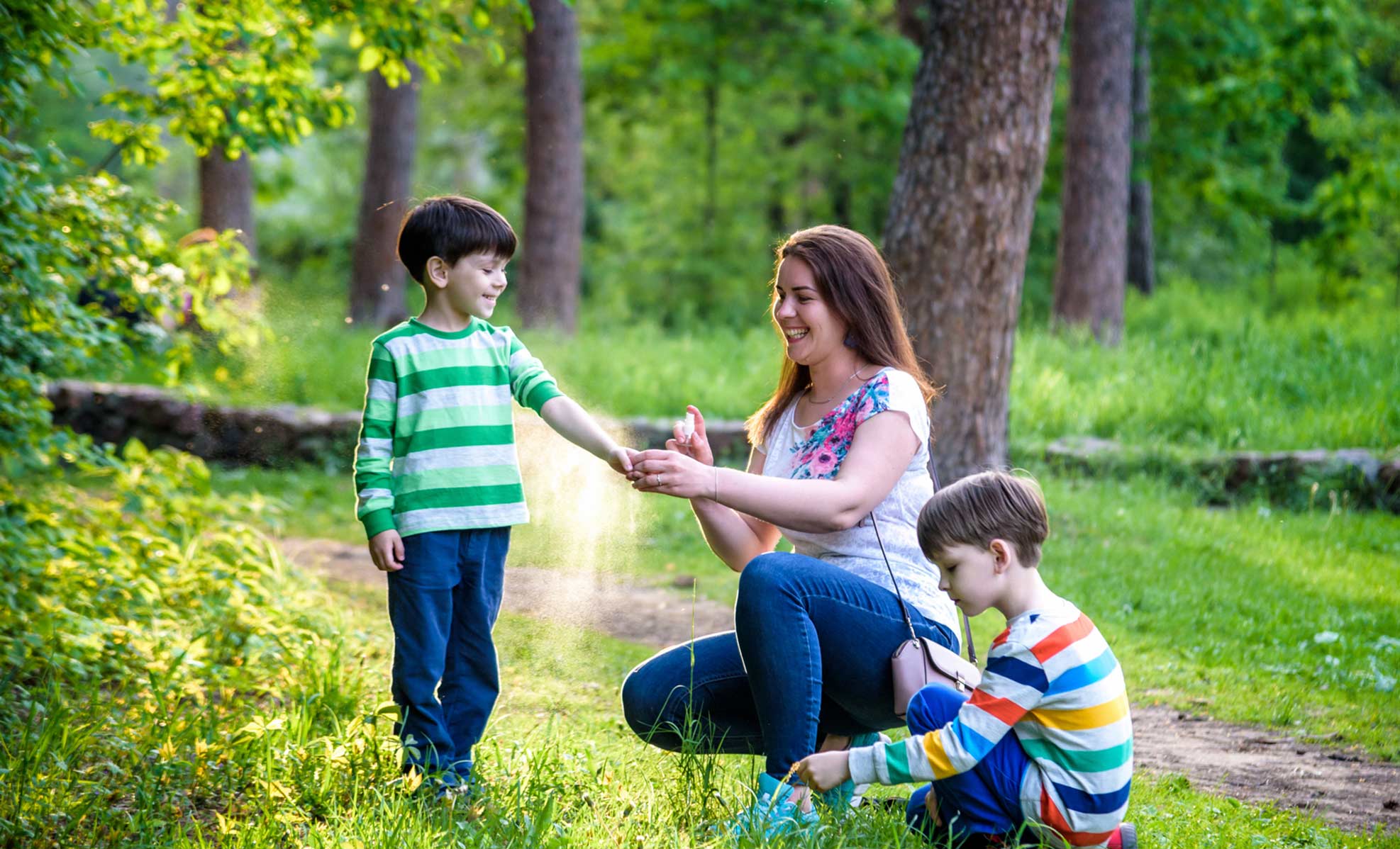 Mom applying deet to her children while walking on a trail