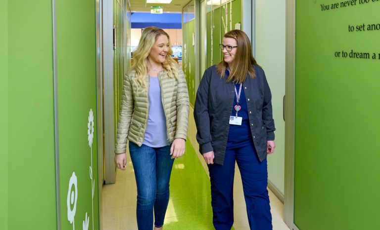 Pediatric nurse walking down the hall with teen girl to exam room