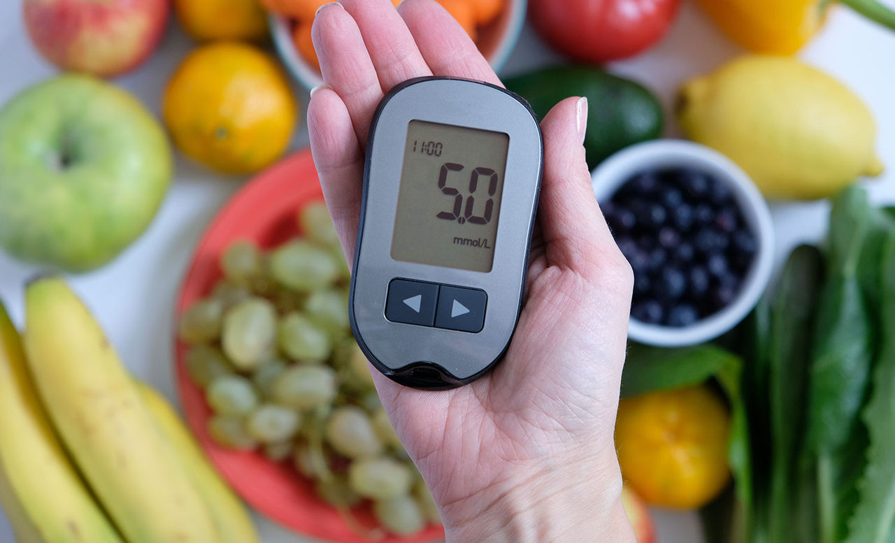 Glucose testing device in hand with healthy foods nearby, highlighting nutrition and diabetes care